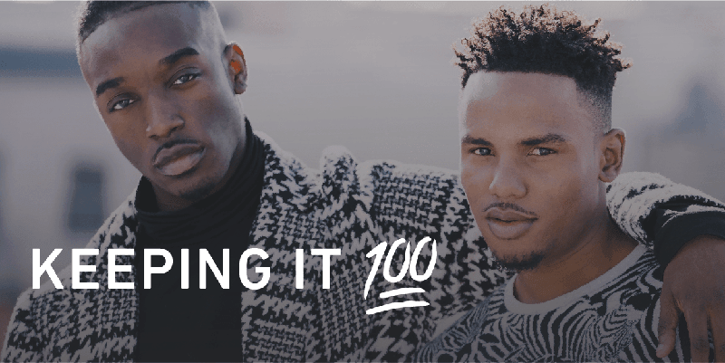 2 African American men standing together with one arm around the other. Both men are wearing trending clothes and are posing for the camera